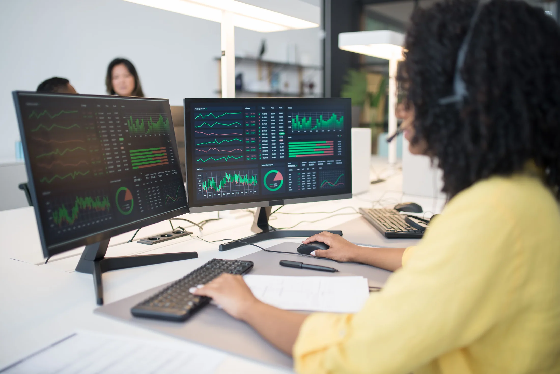 A headset-wearing analyst working in front of dual screens displaying financial data